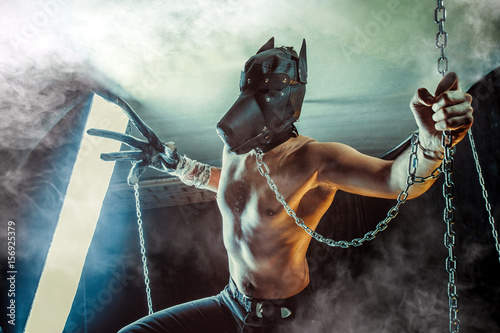 Man in the dog mask on the chain. Dark background.