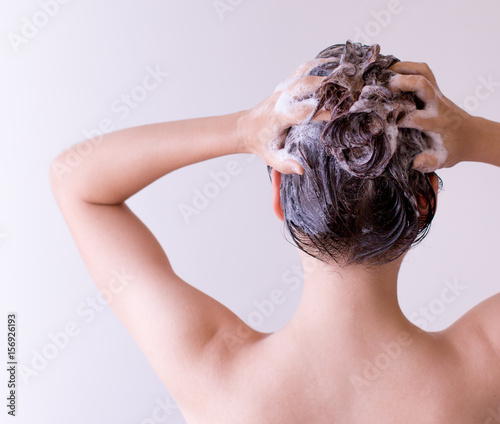 Woman shampoos hair close up with both hands on a white background