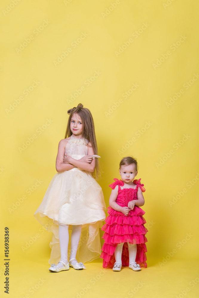 Two sisters in dresses on a yellow background look in different directions and offended Two sisters in dresses on a yellow background look in different directions and offended