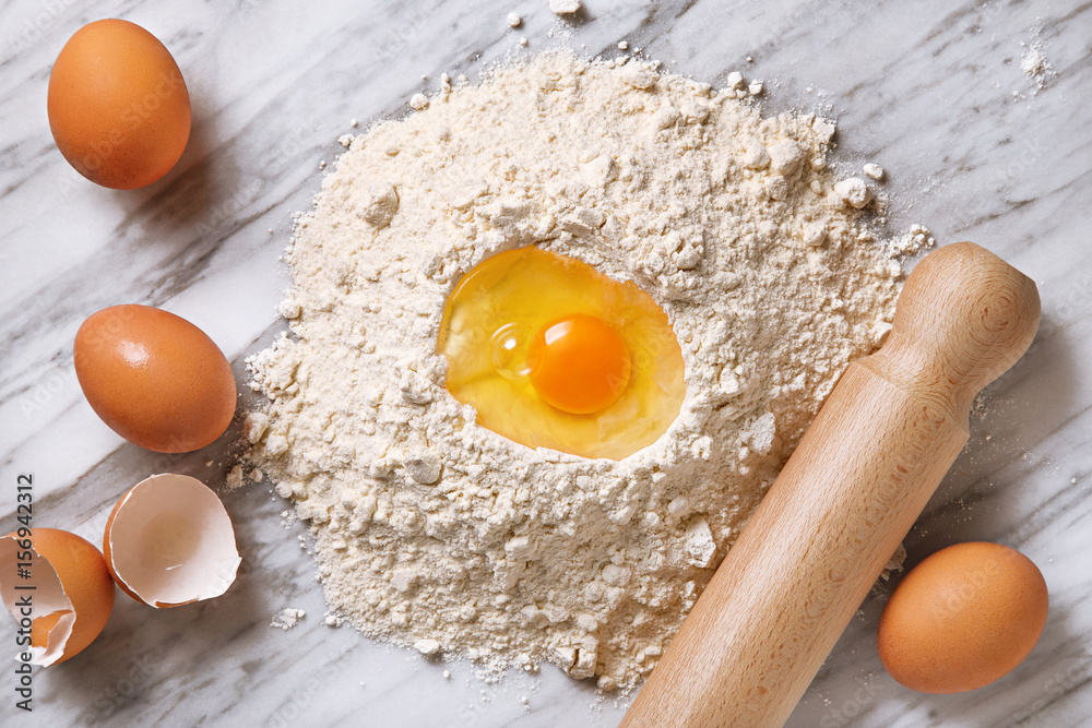 Pasta ingredients. Flour, eggs and rolling pin viewed from above on a marble table. Preparing pasta dough. Top view Pasta ingredients. Flour, eggs and rolling pin viewed from above on a marble table. Preparing pasta dough. Top view