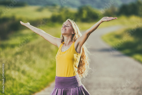 Happy woman standing at the country road with her arms raised.