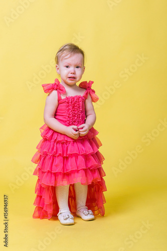 Girl toddler in a pink dress on a yellow background in the Studio