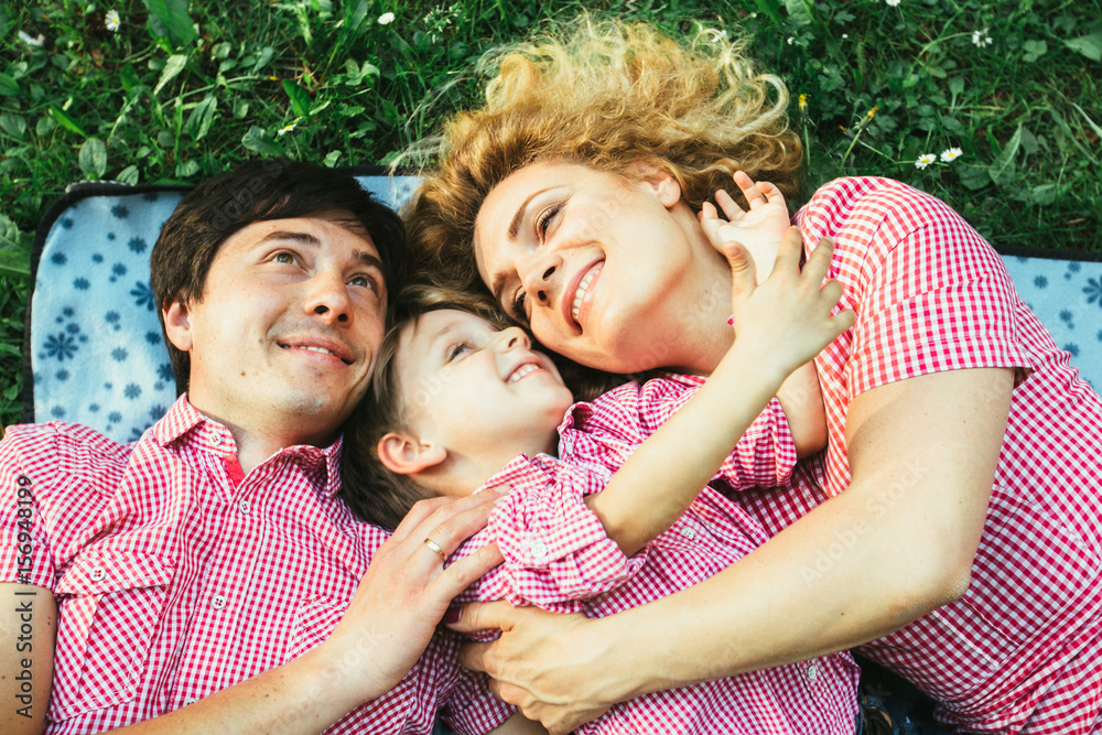 Unique perspective of happy european family smiling while lying down on the green grass in the park Unique perspective of happy european family smiling while lying down on the green grass in the park