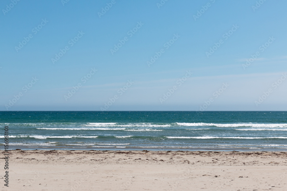 Empty beach with white sand, deep blue water and blue sky