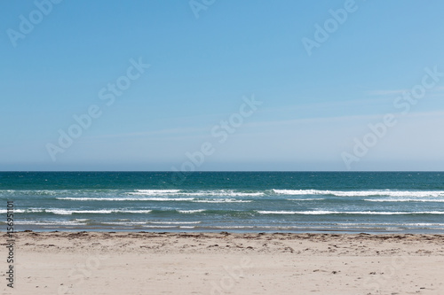 Empty beach with white sand, deep blue water and blue sky