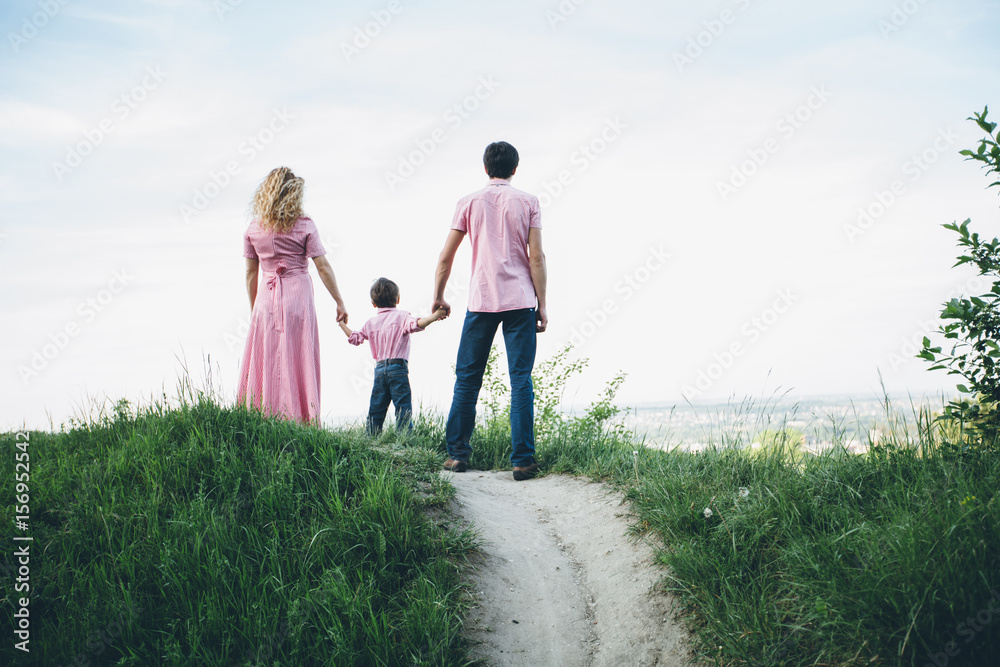 Family of thrree: little boy, father and mother standing on the hill and hilding hands. Back view, full body. Future, looking-for, life concept. Family of thrree: little boy, father and mother standing on the hill and hilding hands. Back view, full body. Future, looking-for, life concept.