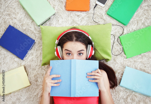 Beautiful young woman lying on floor and listening to audiobook photo