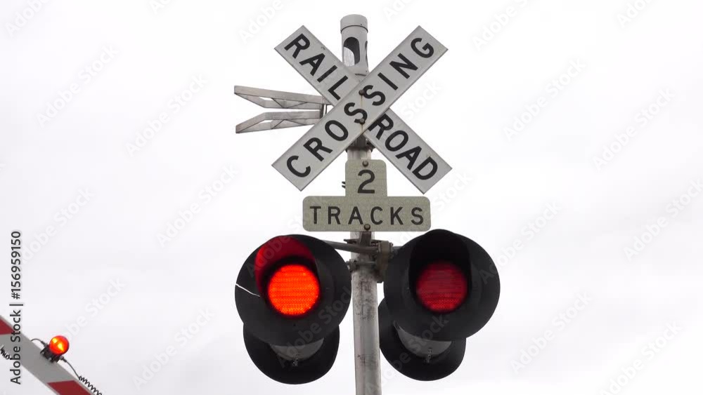 CLOSE UP: Isolated railroad crossing traffic sign with flashing red lights and barrier lowering indicating that a train is coming. Traffic symbols on a intersection of a car road and a railway tracks