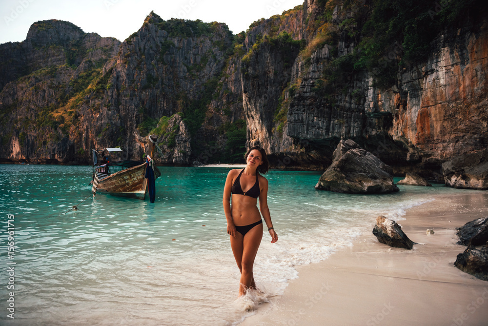 Young tan model on the Maya beach posing wearing bikini with clear water and mountain background, Phi Phi, Thailand