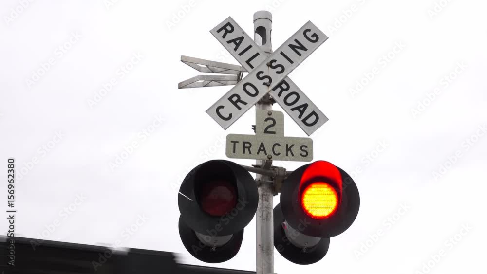 CLOSE UP, POV: Looking at the railroad tracks, the freight train rushing by and the lowered gates with blinking red lights symbolizing stop sign at the intersection of a road and a railway in USA