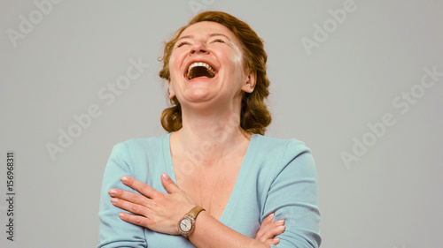 Mid aged actress laughing in s shot. Actress in studio laughing. Close up portrait of an actrees in light blue jumper. Actress with curly red hair laughs. Laughing woman. photo