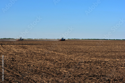 Two tractors sow grain in the field of black earth, sunny spring day, Ukraine