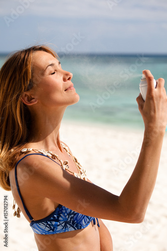 femme à la plage en maillot qui se rafraichit avec brumisateur d'eau