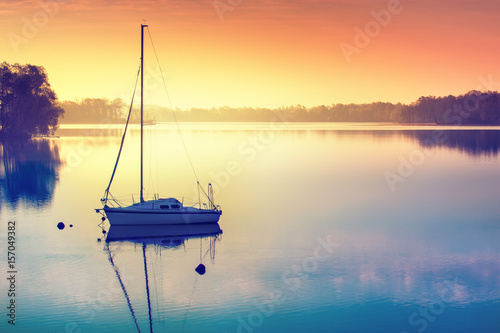 Little sailing boat reflects in the serene water during sunrise. Masuria, Poland.