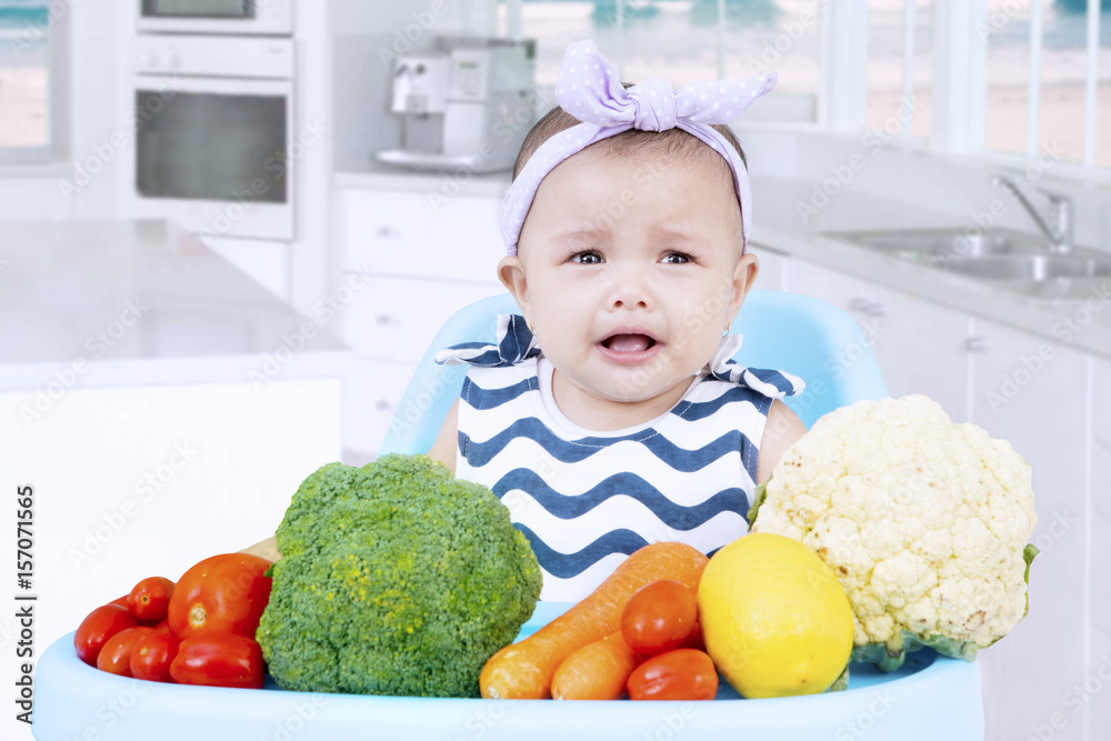 Sad baby with vegetables in kitchen Sad baby with vegetables in kitchen