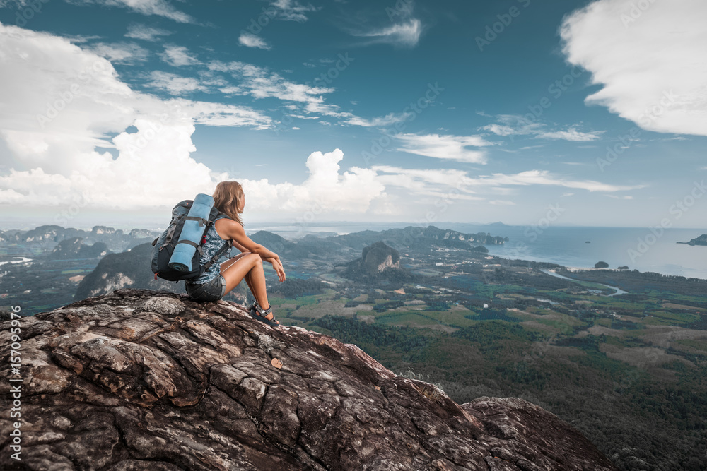 Woman hiker sits on top of a mountain and enjoys valley view