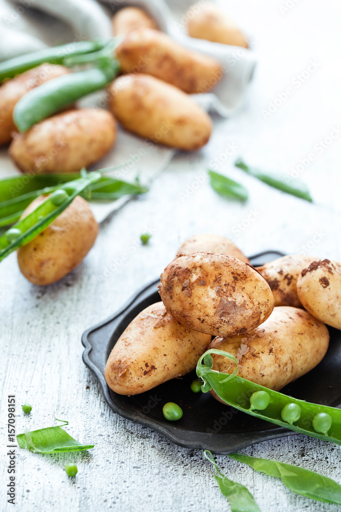 New season raw potatoes with green peas on white wooden background New season raw potatoes with green peas on white wooden background