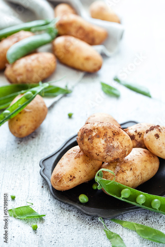New season raw potatoes with green peas on white wooden background