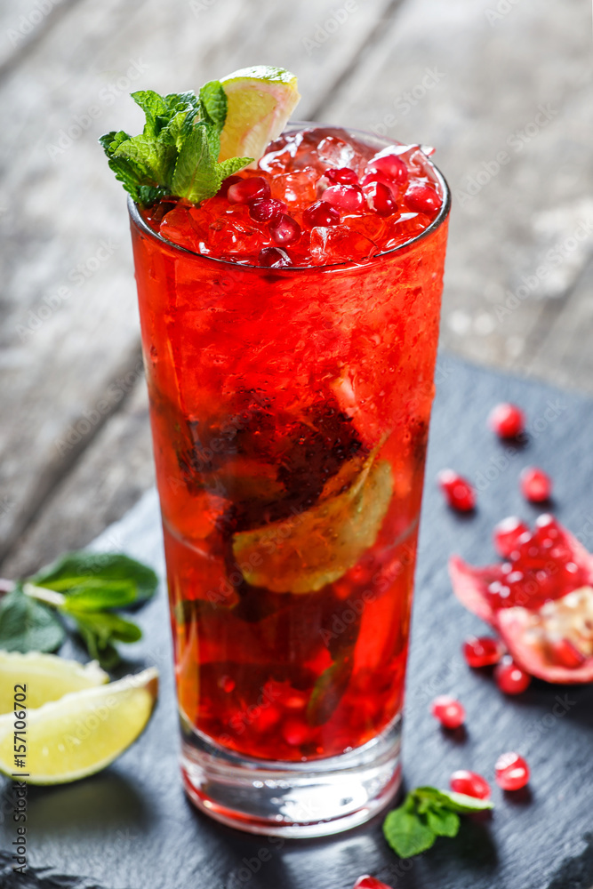 Fresh red lemonade with mint, pomegranate, lime and ice in glass on wooden background. Summer drinks and cocktails Fresh red lemonade with mint, pomegranate, lime and ice in glass on wooden background. Summer drinks and cocktails