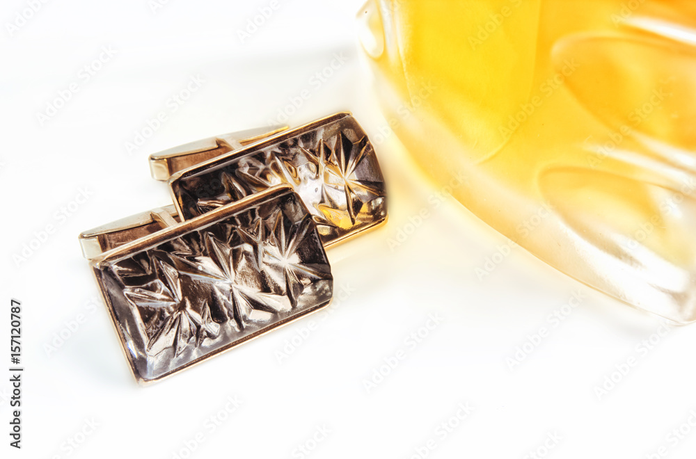 Cuff links on a white background with a bottle of perfume of yellow color. Cuff links on a white background with a bottle of perfume of yellow color.