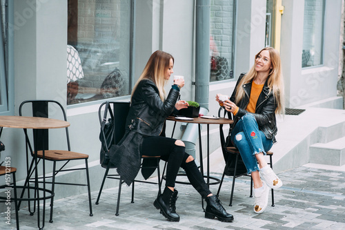 Two beautiful young women drinking coffee and gossiping in nice restaurant outdoor. The weather is great and sunny for walking rest relaxing spending time with best friends!