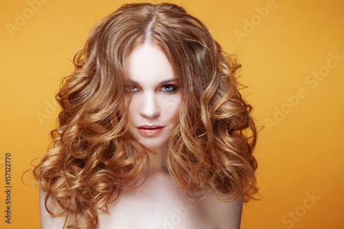 Beautiful redheaded girl with luxurious curly hair. Studio portrait on yellow background. Excellent hair