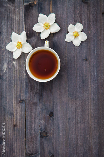 White anime flowers with a cup of tea on a wooden background