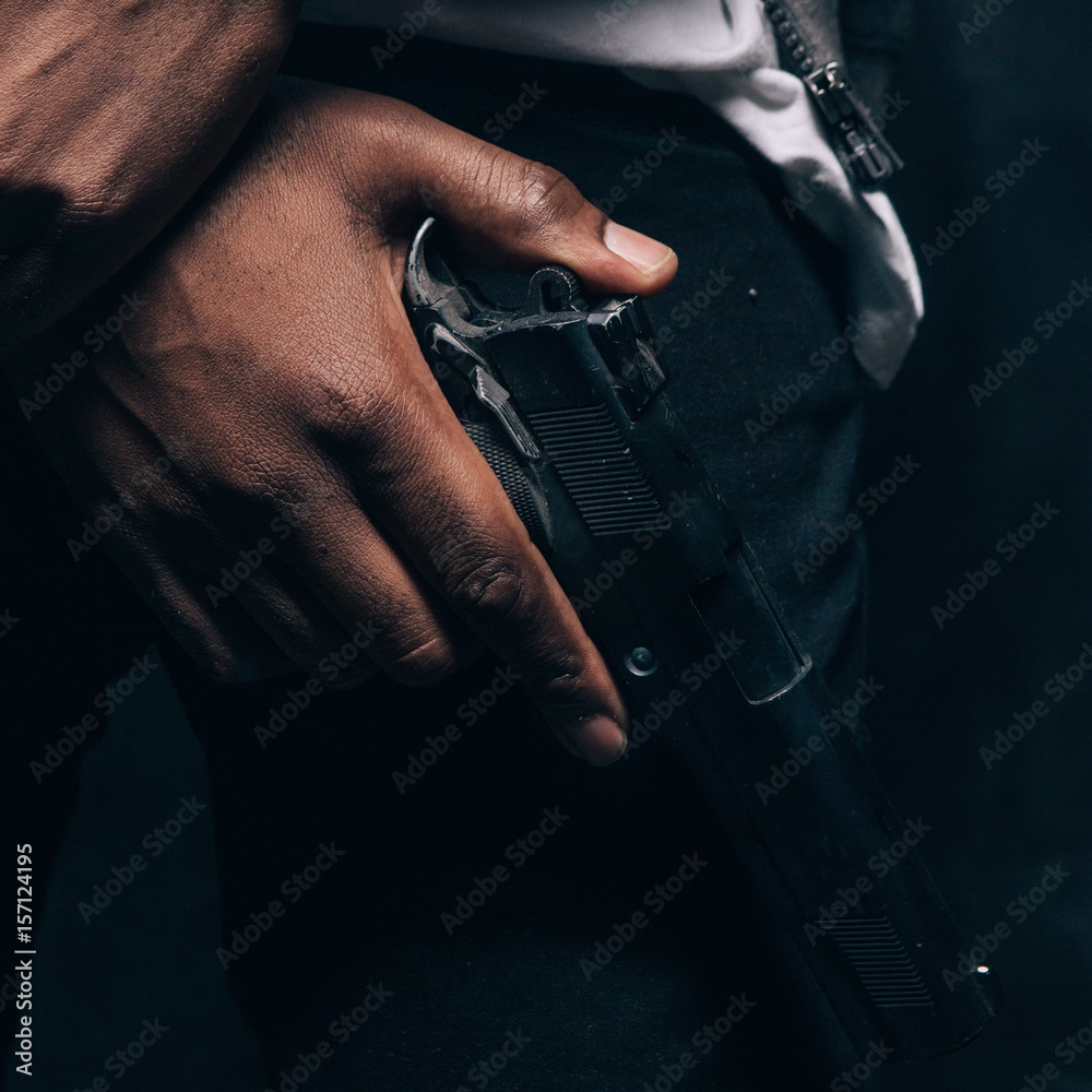 Fotka „Unrecognizable armed black criminal man closeup studio shoot.  Gangster guy with gun in hand on dark background. Outlaw, ghetto, murderer,  robbery concept“ ze služby Stock | Adobe Stock