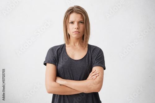 Waist up shot of beautiful irritated young woman with bob haircut holding her arms crossed, having skeptic, angry and annnoyed face, her whole look expressing envy or suspicion. Body language