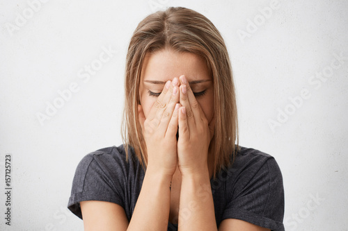 Young female dressed casually covering face with both hands, feeling nervous or ashamed, not looking at camera, hiding herself. Human facial expressions, emotions, feelings, reaction and attitude