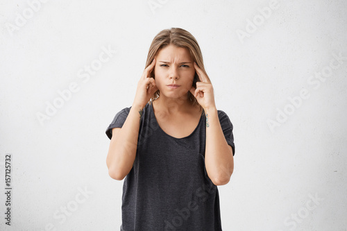 Isolated portrait of frustrated stressed out young mixed race female dressed in dark casual t-shirt holding fingers on her temples as if trying to remember something very important. Body language