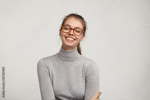 Positive human facial expressions, emotions, reaction and feelings. Fashionable cheerful young female in eyewear closing eyes, laughing from the bottom of her heart, holding hands on stomach