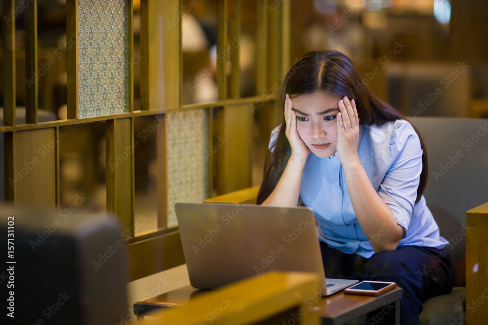 Woman using laptop in cafe at night time and she feel worried
