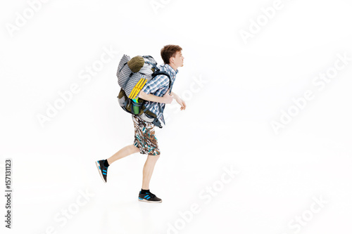 Young tourist with backpack running on white background. hiker was late