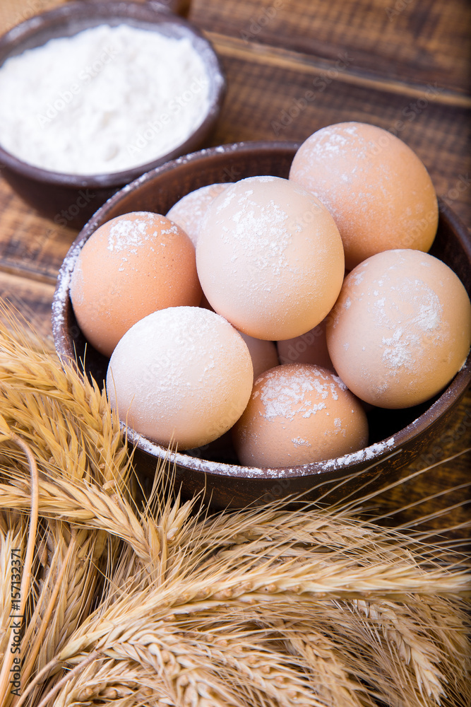 Fresh eggs in a brown bowl, wheat and flour on wooden background. Close-up Ingredients for bakery.