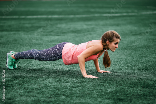 A beautiful muscular girl in tights and a vest makes a warm-up at the stadium. Cross fit, fitness, healthy lifestyle