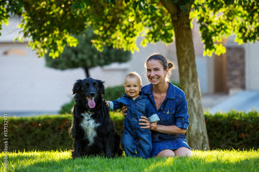 Fototapeta premium A mother with baby son and black dog in green neighborhood