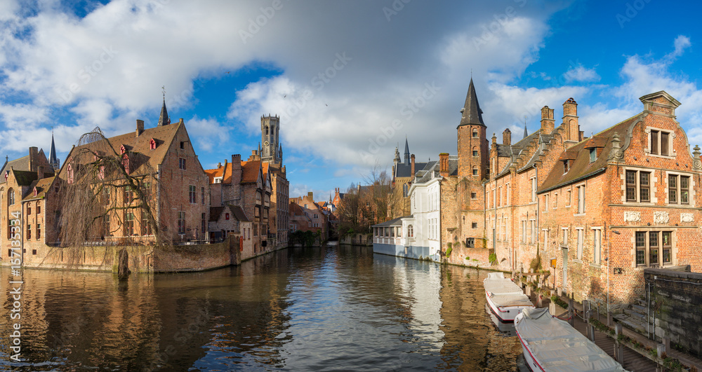 Morning Bruges,Belgium.Image In Realistic Color with Rozenhoedkaai in Brugge,Dijver river canal with Belfort (Belfry) tower.Flanders landmark.Panoramic scenic view with two white boats and cloudy sky
