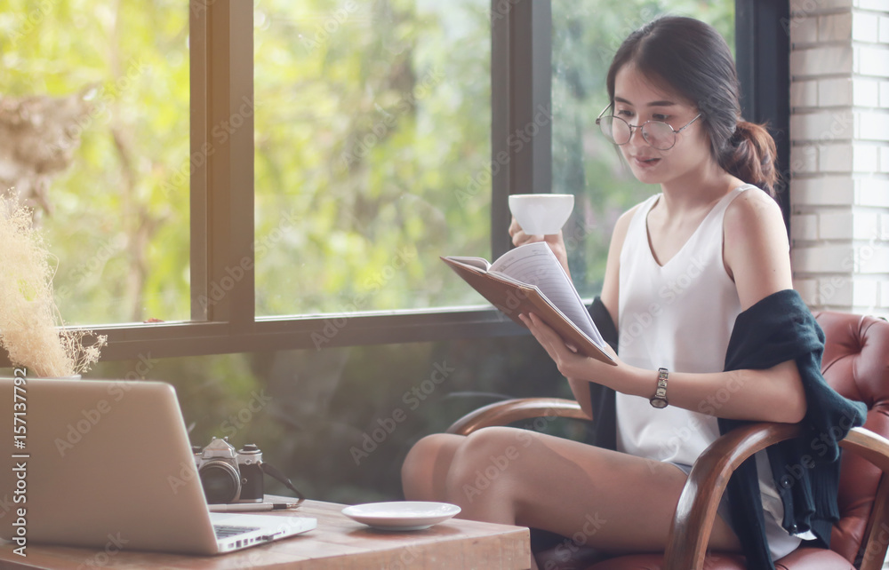 woman reading a book at the wooden counter desk in coffee shop with smile face in happy motion on blurred coffee shop view background under window light woman reading a book at the wooden counter desk in coffee shop with smile face in happy motion on blurred coffee shop view background under window light