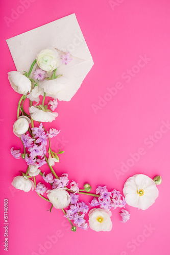 Flowers and paper envelope on pink background. Flat lay, top view. Pattern made of spring flowers