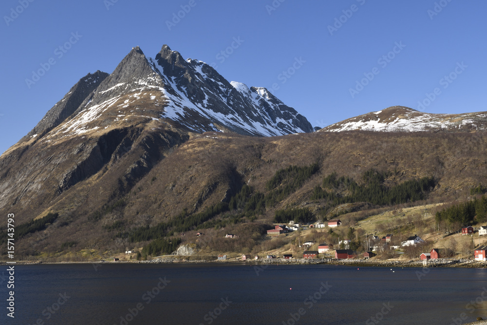 The village Bratland in Norway with high mountains in background against a clear blue sky.