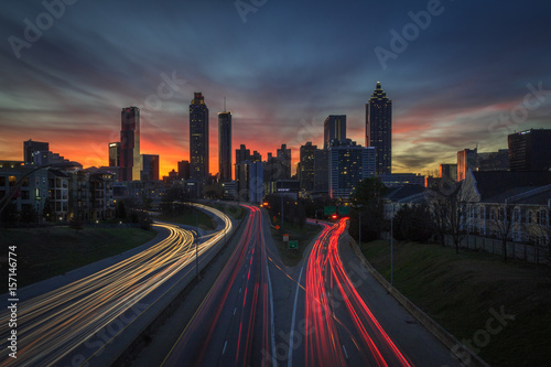 Long Exposure orange, pink, red, blue, purple sunset behind the Atlanta skyline from Jackson Street Bridge with streaked white and red car lights (company names have been edited out) photo
