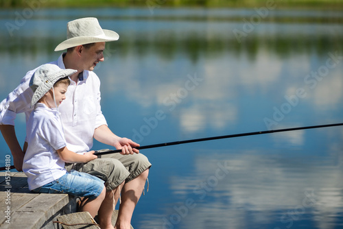 Dad and son are sitting on the pier and fishing on the river