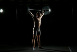 Fitness training. Man standing with barbell in dark gym.