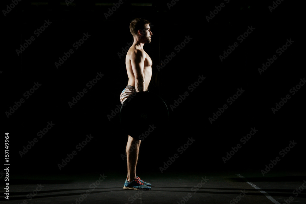 Fitness training. Man doing exercises or training with barbell in dark gym.