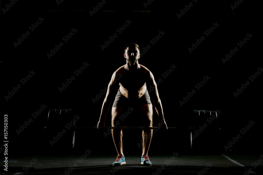 Fitness training. Man doing exercises or training with barbell in dark gym.