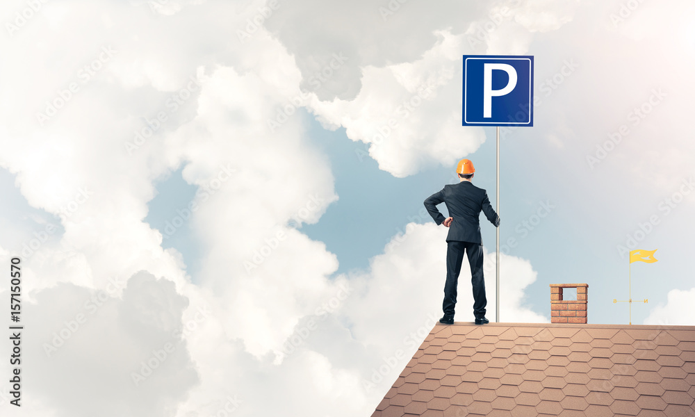 Fototapeta premium Young businessman with parking sign standing on brick roof. Mixe