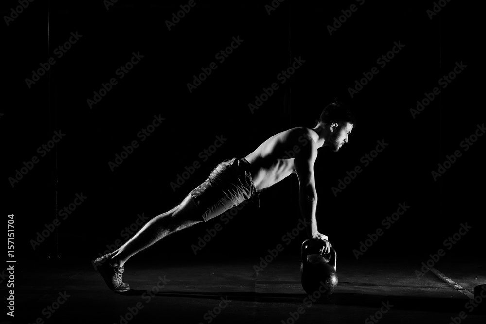 Fitness training. Man doing push ups exercise using dumbbells or weights in dark gym.
