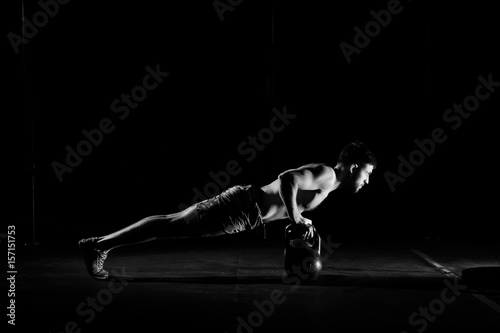 Fitness training. Man doing push ups exercise using dumbbells or weights in dark gym. © Dmitry Tsvetkov