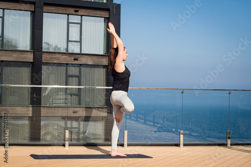sport woman doing stretching yoga exercise on hotel roof with wooden floor stand on yoga mat